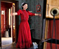 a woman in a red dress is standing by a door and holding her arms out