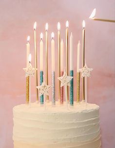 a birthday cake with white frosting and gold stars on top, lit by candles