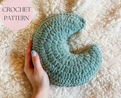 a hand holding a blue crochet heart on top of a white blanket with the words crochet pattern below it