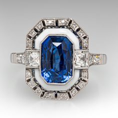 This fabulous Art Deco inspired ring is centered with one (1) cut-cornered rectangular cut natural sapphire that is bordered with white enamel. The ring is accented with two (2) square French cut diamonds, and twenty-two (22) bead set round brilliant and old European cut diamonds. The ring is bordered with milgrain edging. It measures 16.2mm at the top, rises 6.8mm above the finger, tapering to 1.9mm wide and 1.1mm thick at the base of the shank. It is currently a size 7. Elegant Rectangular Enamel Jewelry, White Sapphire Art Deco Jewelry, White Art Deco Baguette Cut Jewelry, White Emerald Cut Art Deco Jewelry, Luxury White Rectangular Ring, Luxury Sapphire Ring With Rectangular Center Stone, White Enamel Ring For Formal Occasions, Formal White Enamel Gemstone Ring, White Rectangular Platinum Jewelry