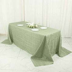 a green table cloth with white plates and flowers on it, sitting in front of a curtained wall