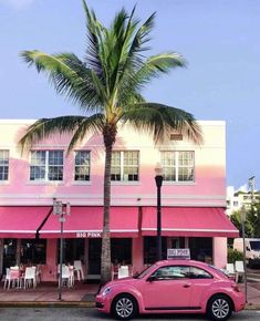 a pink car parked in front of a building with a palm tree on the corner