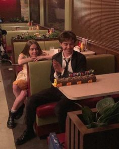 a man and woman sitting at a table in a restaurant with a cake on it