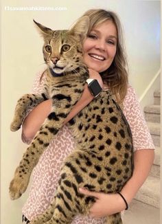 a woman holding a cat in her arms and smiling at the camera while standing next to stairs