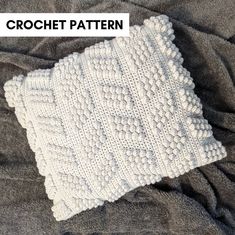 a white crochet blanket sitting on top of a bed next to a pillow