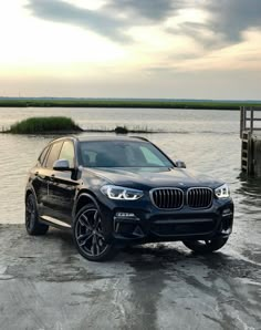 a black bmw suv parked in front of a body of water