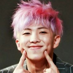 a young man with pink hair is smiling and making a hand gesture to the camera