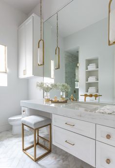 a white bathroom with gold accents and marble counter tops, along with two stools