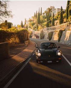 a black sports car driving down a road next to some trees and bushes on the side of a hill