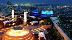 an outdoor dining area overlooking the city lights at night, with tables and chairs set up for dinner