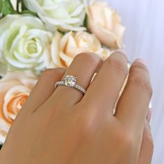 a woman's hand with a diamond ring on it and flowers in the background