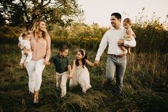 a group of people holding hands and walking through the grass with two children in their arms