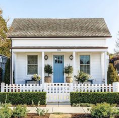 a white house with a blue door and two potted plants on the front porch