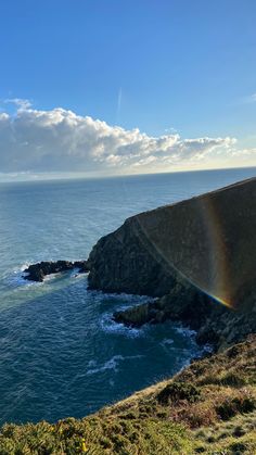 a rainbow shines in the sky over an ocean with cliffs and grass on either side