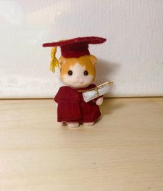 a small stuffed animal wearing a red graduation gown and holding a white piece of paper