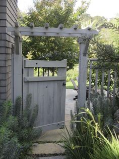 an open gate leading to a house with trees in the back ground and bushes on either side