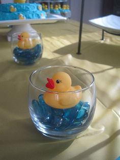 a rubber ducky floating in a clear bowl filled with blue glass pebbles on top of a table