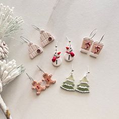 six christmas themed earrings sitting on top of a white table next to a pine tree