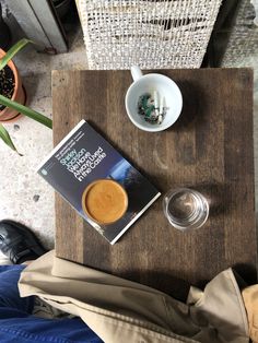 there is a coffee cup and book on the table next to some cups with saucers