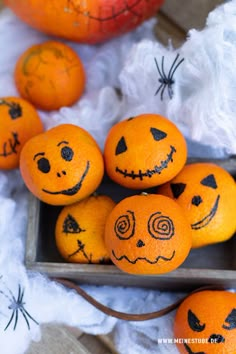 several oranges with faces drawn on them sitting in a wooden box next to other pumpkins