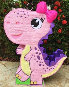 a pink dinosaur with a bow on it's head sitting in front of some bushes