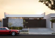 a red car is parked in front of a modern house at sunset or sunrise time