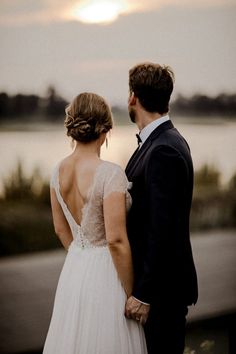 a man and woman standing next to each other in front of the ocean at sunset