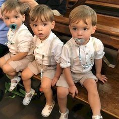 three little boys sitting on a bench with pacifier in their mouth and wearing white shoes