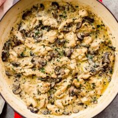 a pan filled with chicken and mushrooms on top of a red cloth next to a wooden spoon