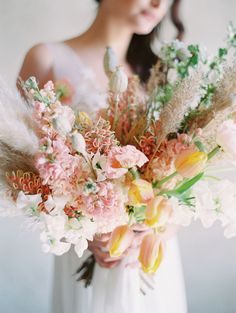 a woman in a white dress holding a bouquet of flowers and feathers with her face close to the camera