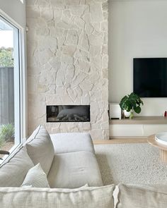 a living room with white furniture and a stone wall behind the fireplace in front of a flat screen tv