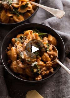 two black bowls filled with pasta and broccoli on top of a gray cloth