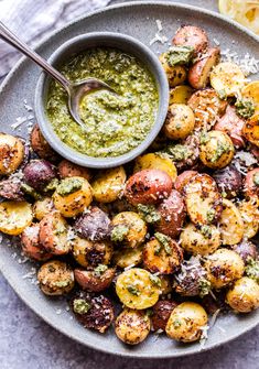 roasted potatoes with pesto sauce and parmesan cheese on a plate next to a lemon wedge