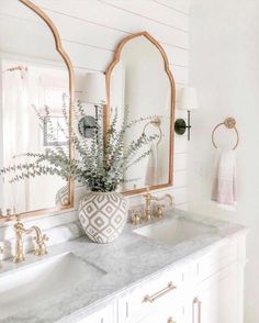 a bathroom with two sinks, mirrors and plants in the vase on the counter top