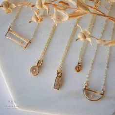 four gold necklaces sitting on top of a white marble table next to dried flowers