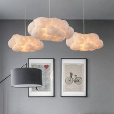 three white clouds hanging from the ceiling above a bed in a room with two pictures on the wall