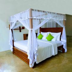 a bed with white linens and green pillows in a room that has concrete floors