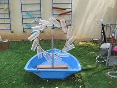 an upside down plastic umbrella in a blue boat on the grass with ladders behind it