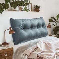 a bed with a blue headboard and pillows on it, next to potted plants