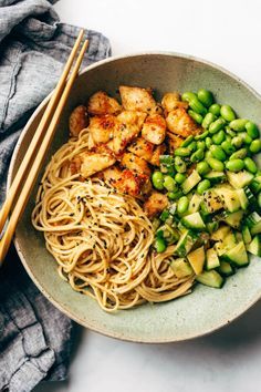 a bowl filled with noodles and vegetables next to chopsticks on a white surface