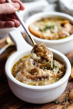 a spoon full of soup on top of a wooden cutting board with bread in the background