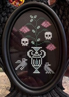 a cross - stitch picture of a vase with flowers in it and skulls on the side