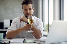 a man sitting at a table with a glass of wine in front of his laptop