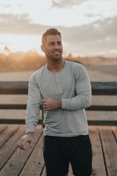 a man standing on top of a wooden pier next to the ocean with his arms crossed