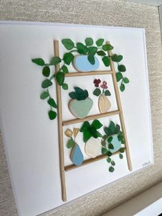 an art piece made out of wood and paper with green leaves on the top, next to a ladder