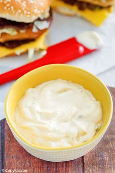 a yellow bowl filled with white sauce next to two hamburgers