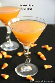 two glasses filled with candy corn martinis on top of a black table next to candy candies