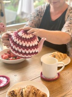 a woman sitting at a table holding a tea pot over a crocheted cup and saucer