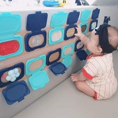 a small child is playing with toys on the floor in front of a wall full of magnets