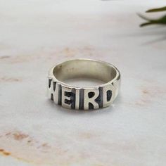 WEIRD Ring in Sterling Silver: Features a 6mm wide band with the word "WEIRD" sculpted onto the surface, curved with the shape of the ring. Where the letters are slightly raised, the profile is about 2.5mm tall. Oxidized to bring out details. Due to the handmade nature of our items, please allow 2-3 weeks for production. Rings With Words, Weird Rings, Word Rings, Weird Accessories, Strange Rings, Weird Products, Fun Rings, Cool Rings, Word Ring